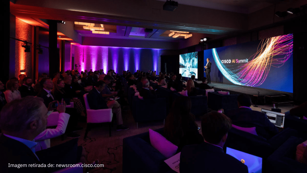 Auditório cheio no Cisco AI Summit 2025, com um palestrante no palco apresentando um slide sobre tecnologia e inovação. A tela exibe o logotipo do evento com gráficos coloridos representando inteligência artificial. O público assiste atentamente, e alguns utilizam notebooks e celulares. Iluminação em tons de roxo e laranja cria um ambiente moderno e tecnológico.