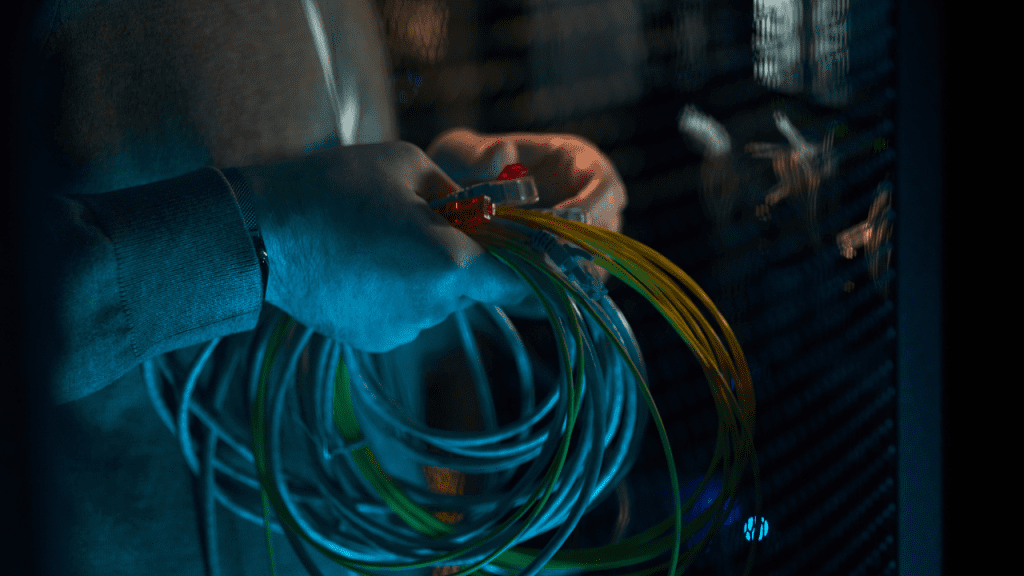 Técnico segurando cabos de rede e fibra óptica em data center, representando infraestrutura de alta velocidade para internet e transmissão de dados.