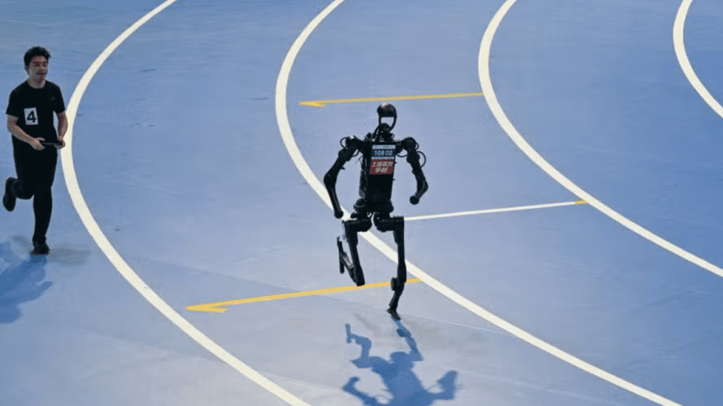 Robô humanoide corre em pista atlética azul, acompanhado por operador humano, durante competição de robótica.