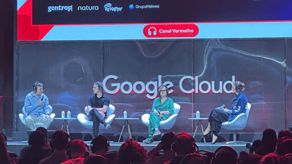Painel no Google Cloud Summit: quatro palestrantes sentados com headsets diante do telão “Google Cloud”; público com fones. No topo, logos de gentrop, Natura, Grupo Ri Happy e Grupo Malwee e indicação “Canal Vermelho”.