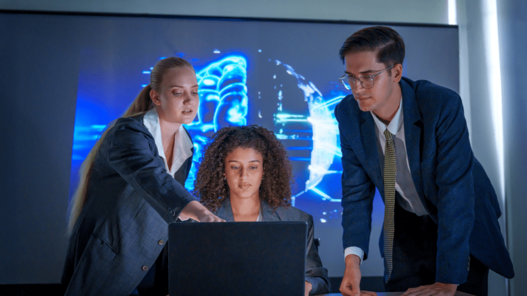 Três profissionais de terno reunidos em frente a um notebook, analisando algo na tela, com um grande display ao fundo exibindo uma imagem digital azul que remete a inteligência artificial e cibersegurança.