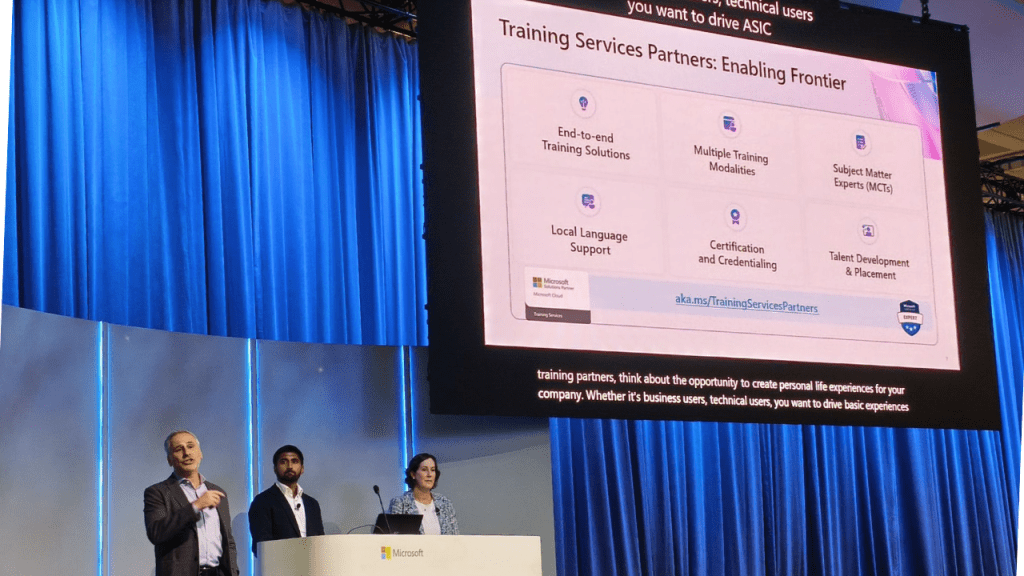 Palestra em um evento da Microsoft, com três apresentadores em um palco diante de cortinas azuis, ao lado de um grande telão que exibe o slide “Training Services Partners: Enabling Frontier”, destacando tópicos como soluções de treinamento de ponta a ponta, múltiplas modalidades de treinamento, suporte em idioma local, certificação e desenvolvimento de talentos.