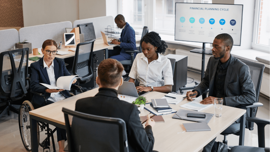 Equipe em reunião no escritório, analisando documentos e laptop, com tela ao fundo exibindo “Financial Planning Cycle