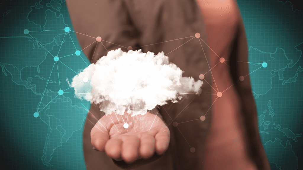 Pessoa com a mão estendida segurando uma nuvem digital flutuante, com conexões em rede e mapa-múndi ao fundo, representando cloud computing, multicloud e tendências de Cloud Foundations para 2026.