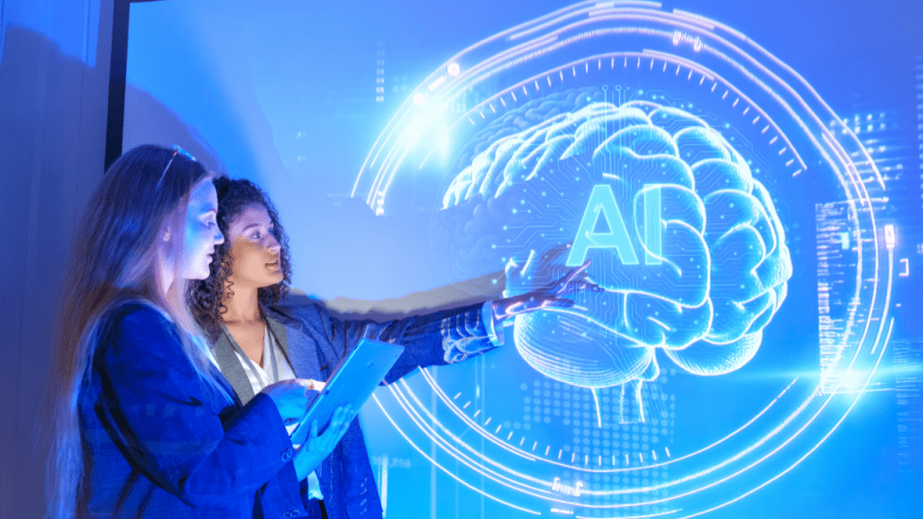 Dos profesionales frente a una pantalla digital azul con un cerebro ilustrado y la palabra “AI”; una señala la proyección mientras la otra sostiene una tablet.