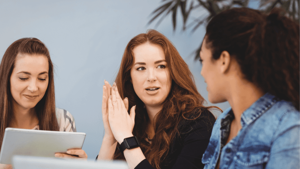 Três mulheres conversando em um ambiente corporativo, representando mentoria feminina, desenvolvimento de lideranças e troca de experiências profissionais nas empresas.