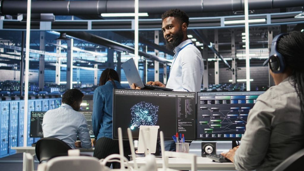 Equipe de segurança monitorando telas em um centro de operações, com visualização de inteligência artificial e dados digitais para análise de ameaças cibernéticas.